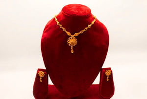 Gold necklace set with spiral flower pendant, ruby crystal centre and matching flower stud earrings on a red bust