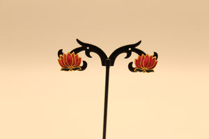 Pink enamel lotus stud earrings with green leaves and gold edging on a display stand