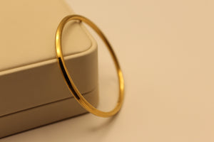 Slim gold-polished silver bangle with square-edge profile leaning on a jewellery box